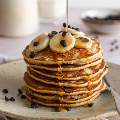 a stack of pancakes with banana slices and chocolate chips on top and maple syrup on top