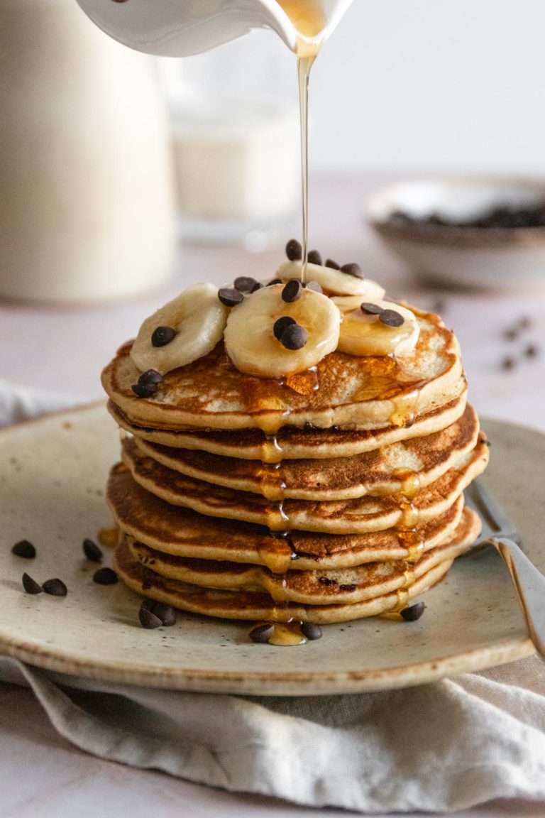 a stack of pancakes with banana slices and chocolate chips on top and maple syrup on top