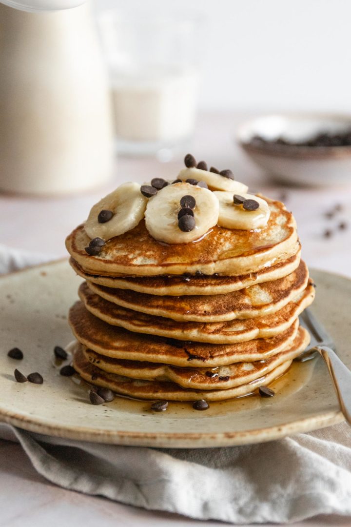 a stack of pancakes with banana slices, chocolate chips and maple syrup on top