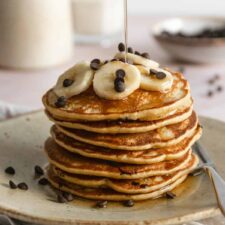 a stack of pancakes with banana slices and chocolate chips on top and maple syrup on top