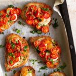 cherry tomato bruschettas on a baking tray with chopped basil on top