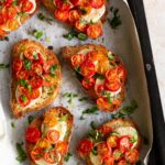a baking tray with bread slices with goat cheese, cherry tomatoes and chopped basil