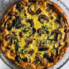 one quiche with mushrooms and spinach on top of a kitchen towel