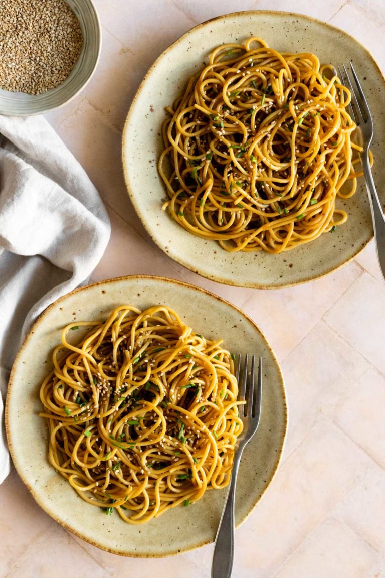 two plates served with noodles, sesame seeds and chopped chives. A small bowl with more sesame seeds on the top left corner