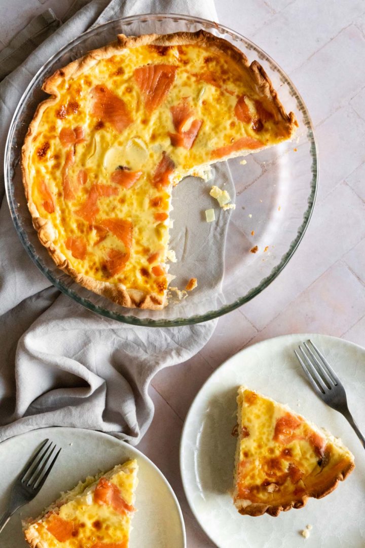 smoked salmon quiche on a glass baking dish, two plates with on slice of quiche each