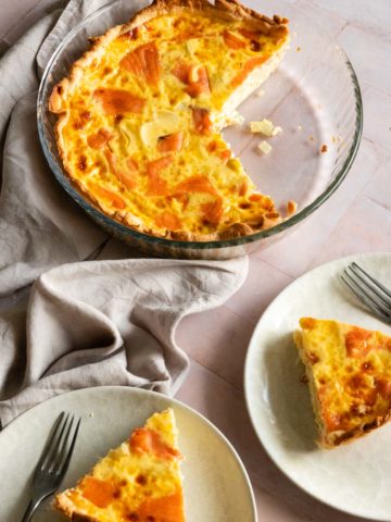 smoked salmon quiche on a glass baking dish, two plates with on slice of quiche each