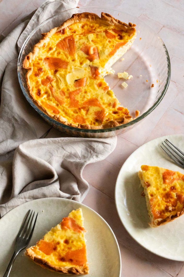 smoked salmon quiche on a glass baking dish, two plates with on slice of quiche each