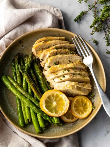 a plate served with sliced chicken breast, lemon slices and cooked asparagus