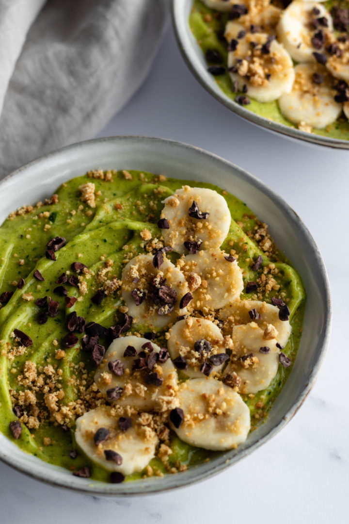 bowl with green smoothie, sliced banana, cacau nibs and peanut crumble