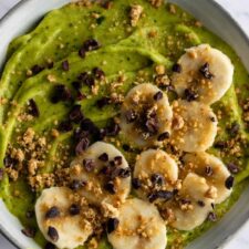 close up of a breakfast bowl with green smoothie, sliced banana, cacau nibs and peanut crumble