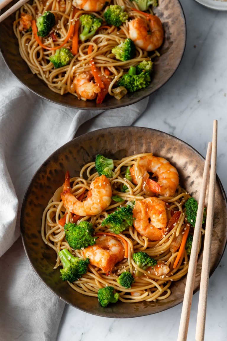 two bowls with noodles, carrot, shrimp, broccoli and sesame seeds on top