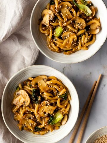 two bowls served with noodles, mushrooms, cabbage and sesame seeds on top