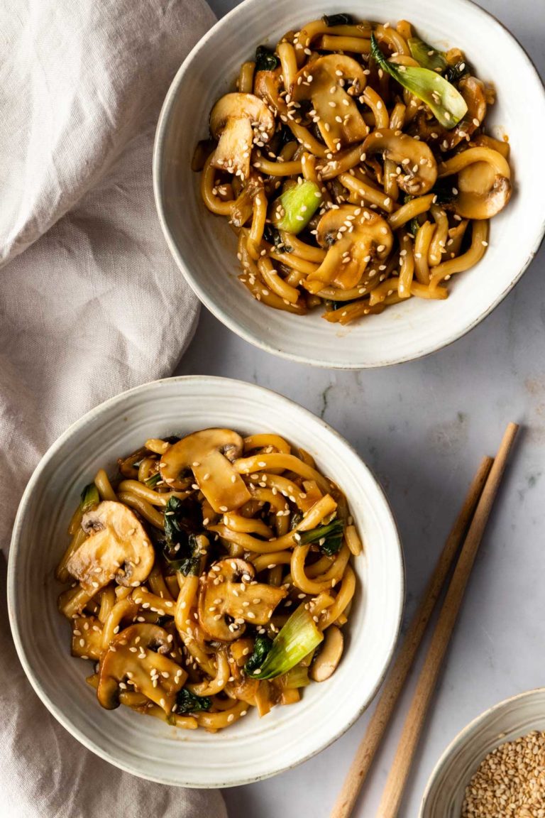 two bowls served with noodles, mushrooms, cabbage and sesame seeds on top