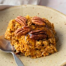 a small plate served with baked oatmeal with a drizzle of maple syrup and a small spoon on the side