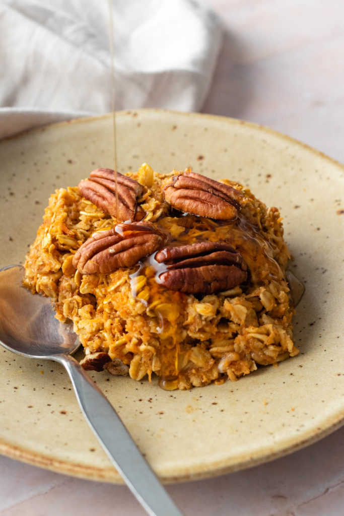 a small plate served with baked oatmeal with a drizzle of maple syrup and a small spoon on the side