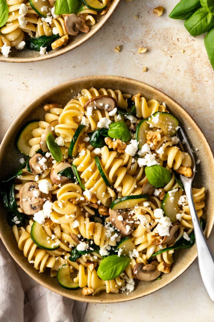 one plate served with pasta, zucchini, mushrooms, spinach, crumbled feta and walnuts.
