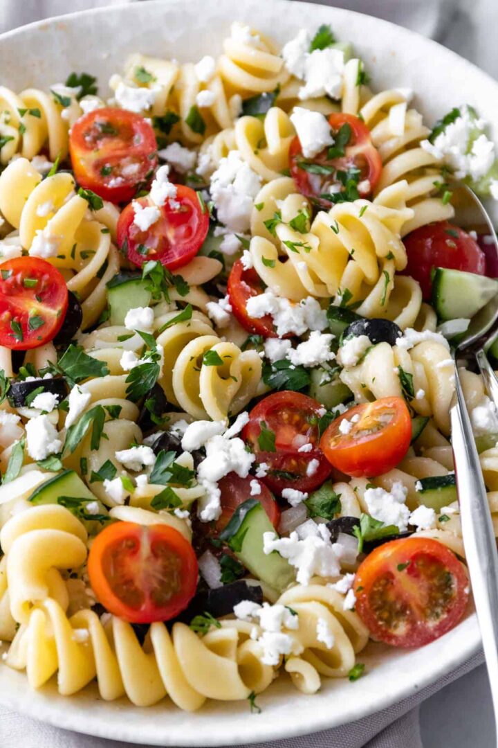 close-up of pasta salad with cherry tomatoes, cucumber, crumbled feta, olives and chopped parsley