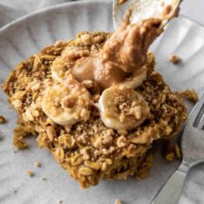 banana oatmeal served on a plate with peanut butter and with a fork on the side