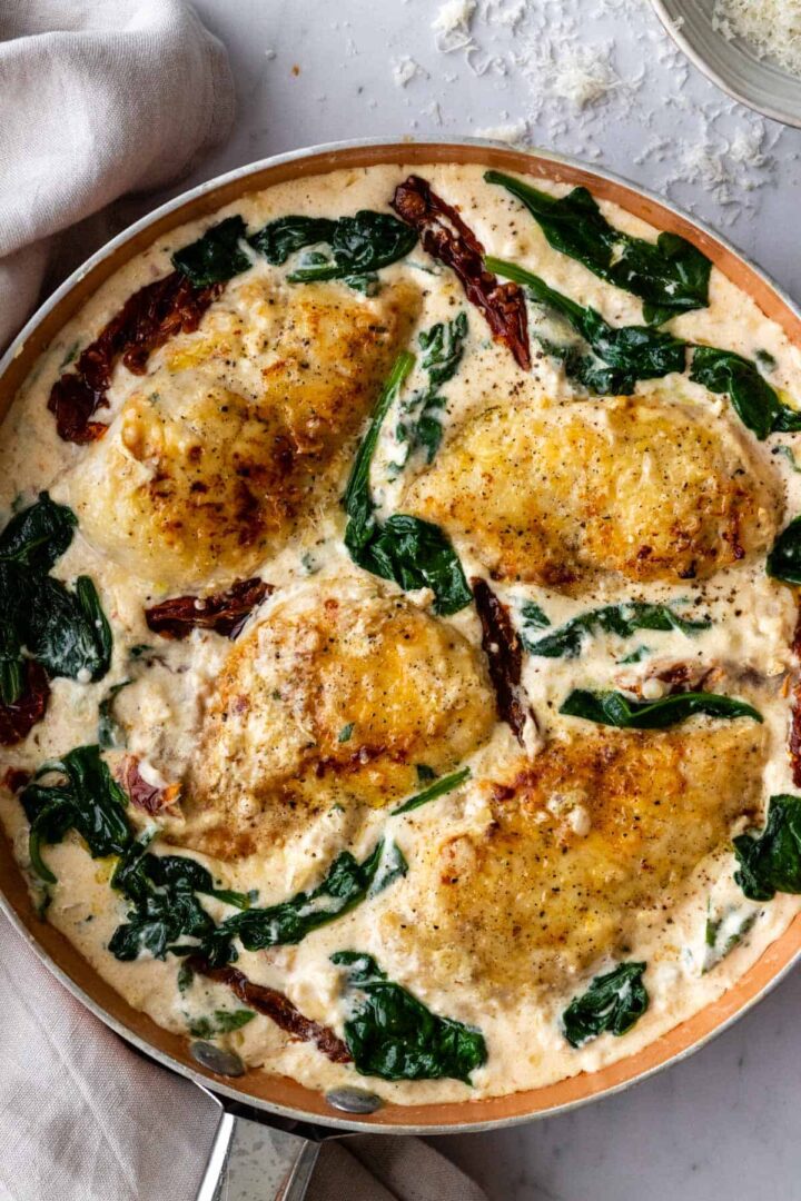 a pan with chicken breasts, spinach leaves, sun-dried tomatoes and cream