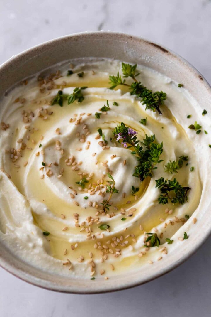 whipped feta dip served on a bowl with honey, sesame seeds, and fresh thyme on top