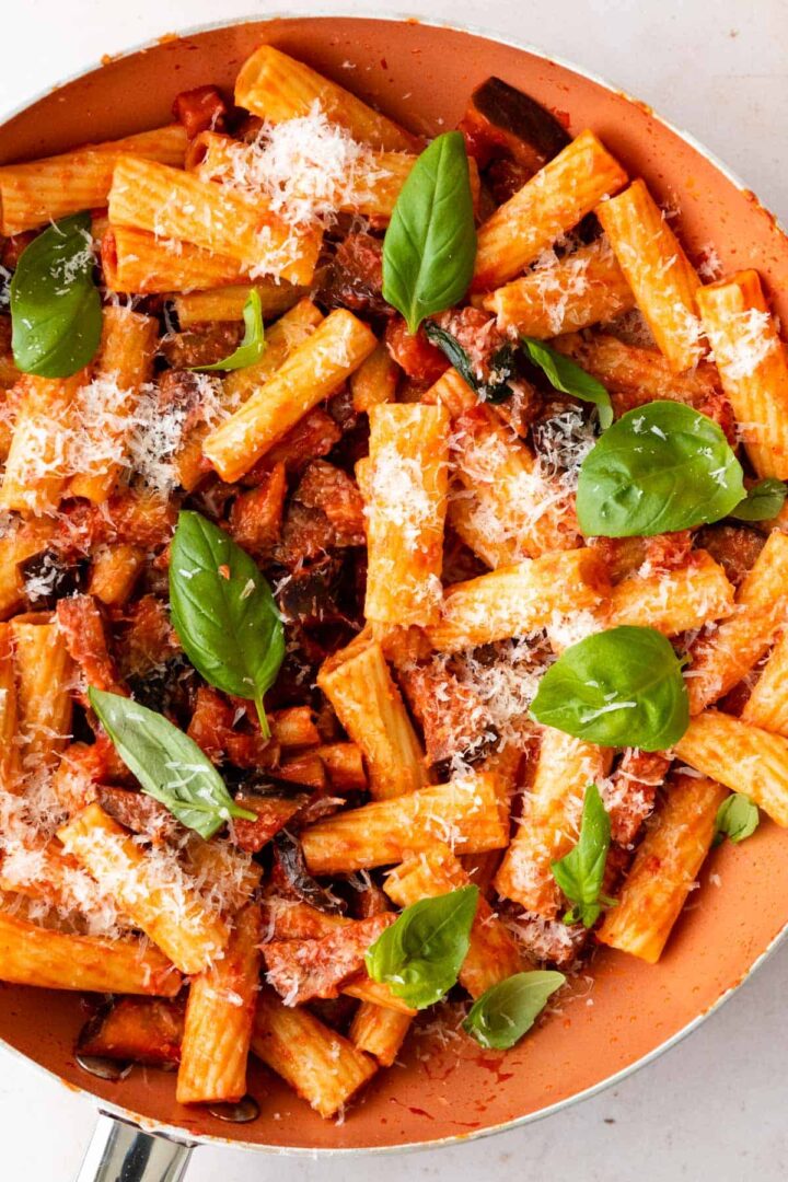 close-up of a pan with pasta, aubergine, tomato sauce, grated parmesan cheese and basil leaves