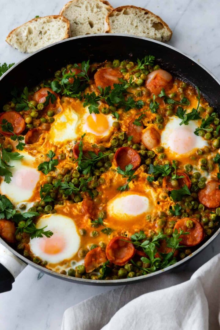 a pan served with peas, eggs, sliced chorizo, coriander and sliced toasted bread served on the side