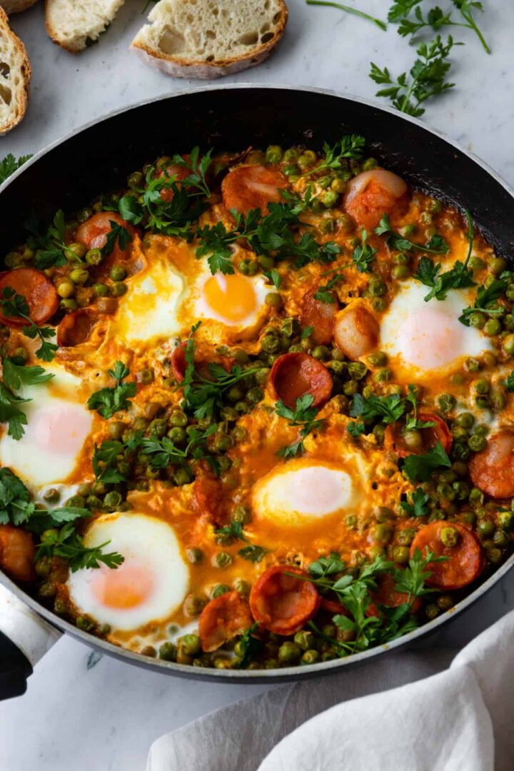 a pan with eggs, sliced chorizo, peas, coriander to garnish and toasted bread on the side