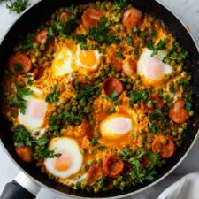 one pan with peas, eggs, chorizo, coriander on top and toasted bread on the side.