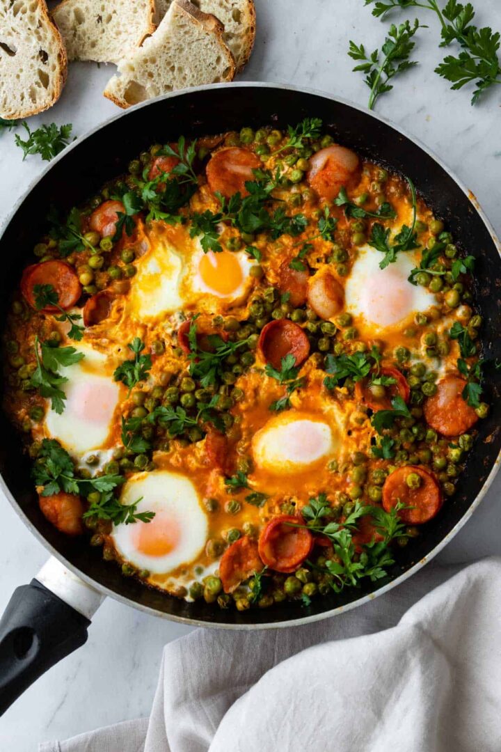 one pan with peas, eggs, chorizo, coriander on top and toasted bread on the side.
