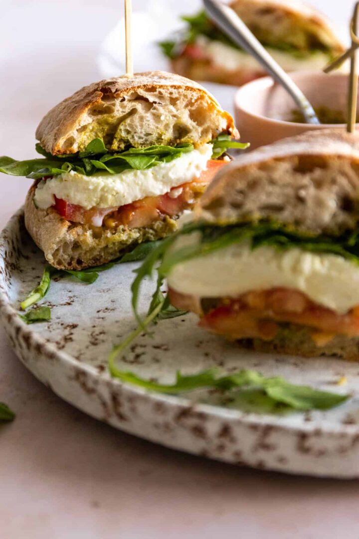 a plate with a dew sandwiches with arugula, mozzarella, tomato, and pesto