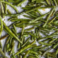 roasted green beans seasoned with salt on a baking tray with parchment paper