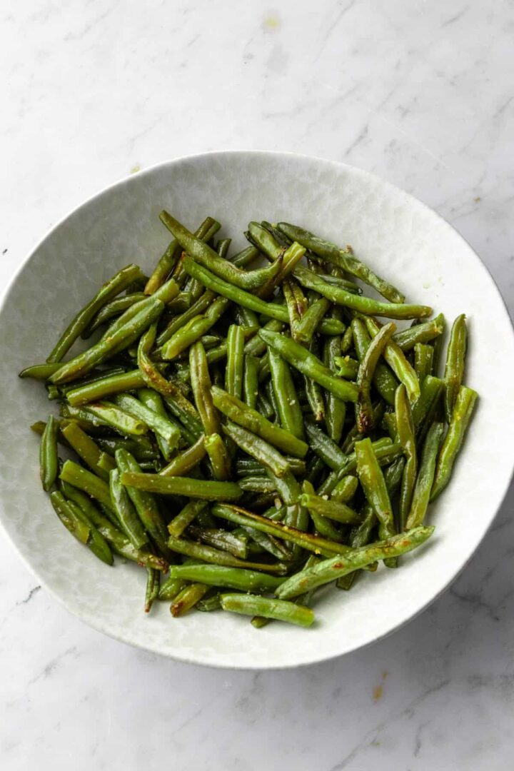 a large bowl with roasted green beans on a marble background