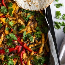 a baking tray with sheep pan chicken fajitas, aka chicken breast slices, bell pepper slices, sliced onion, coriander, and tortillas