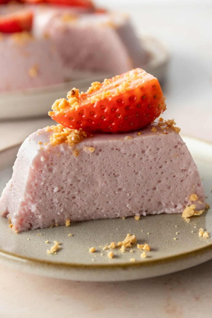 a small plate with a slice of strawberry pudding cake with a slice of strawberry on top and garnished with soft cookie crumbs