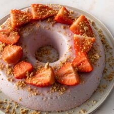one large plate with a strawberry pudding cake with sliced strawberries on top and garnished with soft cookie crumbs