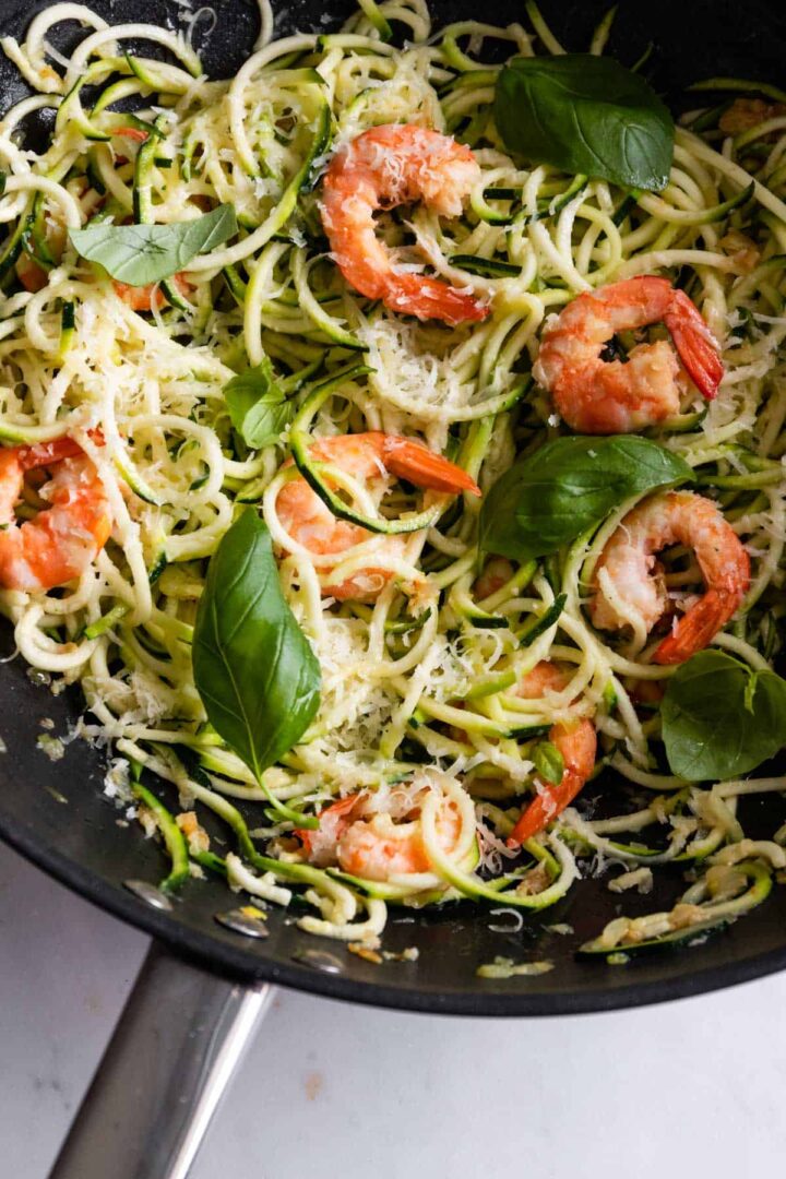 a pan with shrimp and zucchini noodles with basil leaves and parmesan cheese on top