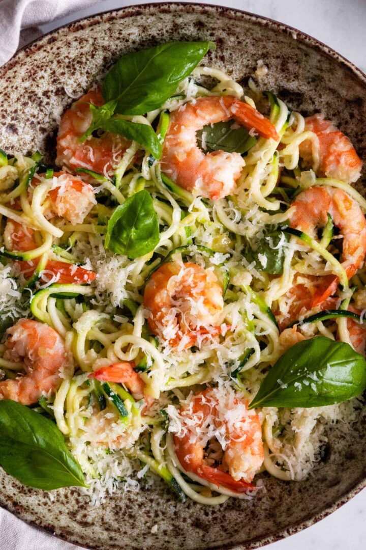 a bowl with zucchini noodles, shrimp, parmesan cheese and basil leaves