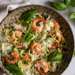 a bowl with zucchini noodles, shrimp, parmesan cheese and basil leaves. More basil leaves on the side