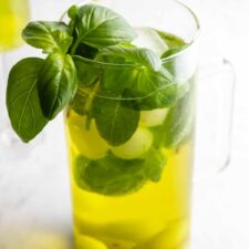 large jug with fresh basil, ice cubs, melon balls, grapes, and sangria
