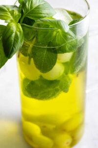 large jug with fresh basil, melon balls, grapes, and ice cubs