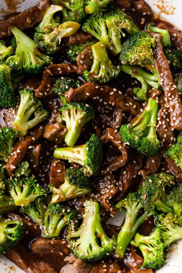 close-up to a pan with broccoli florets, beef, and sesame seeds
