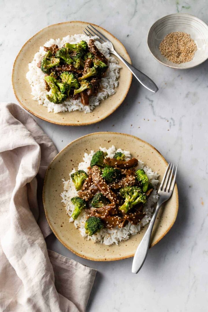 two plates served with beef and broccoli stir fry, a small bowl with sesame seeds on the side