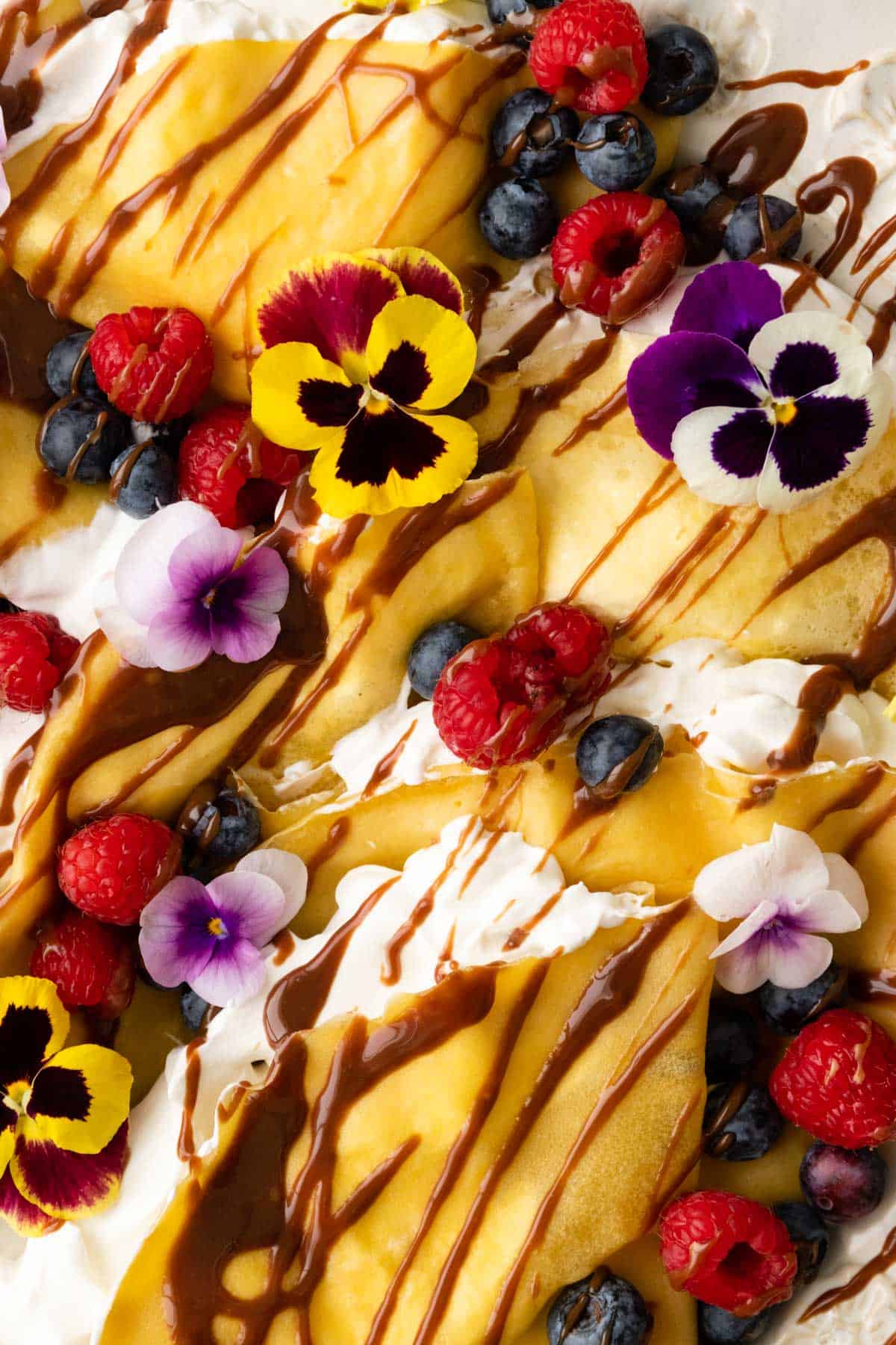 close up to crepes with whipped cream, and garnished with berries, chocolate sauce and flowers