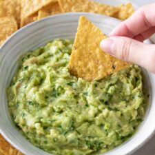 one hand dipping a tortilla chip inside a bowl with guacamole