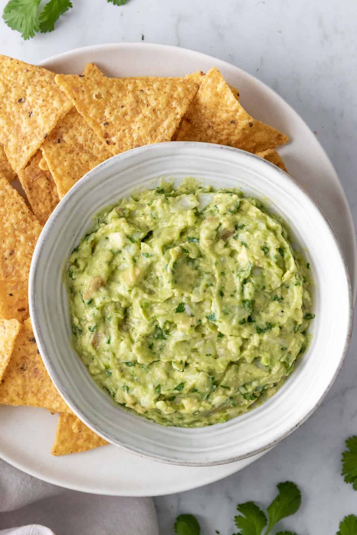 one large plate with tortilla chips and a small bowl with guacamole