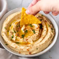 a hand is dipping a chip into the hummus.