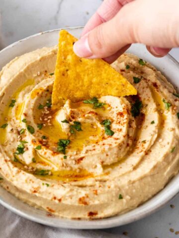 a hand is dipping a chip into the hummus.