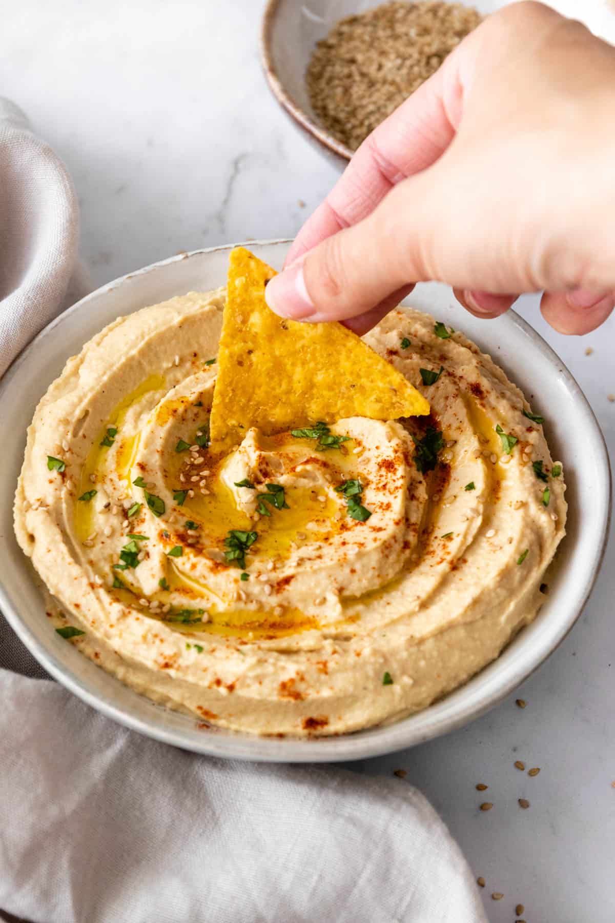 a hand dipping a chip into the hummus