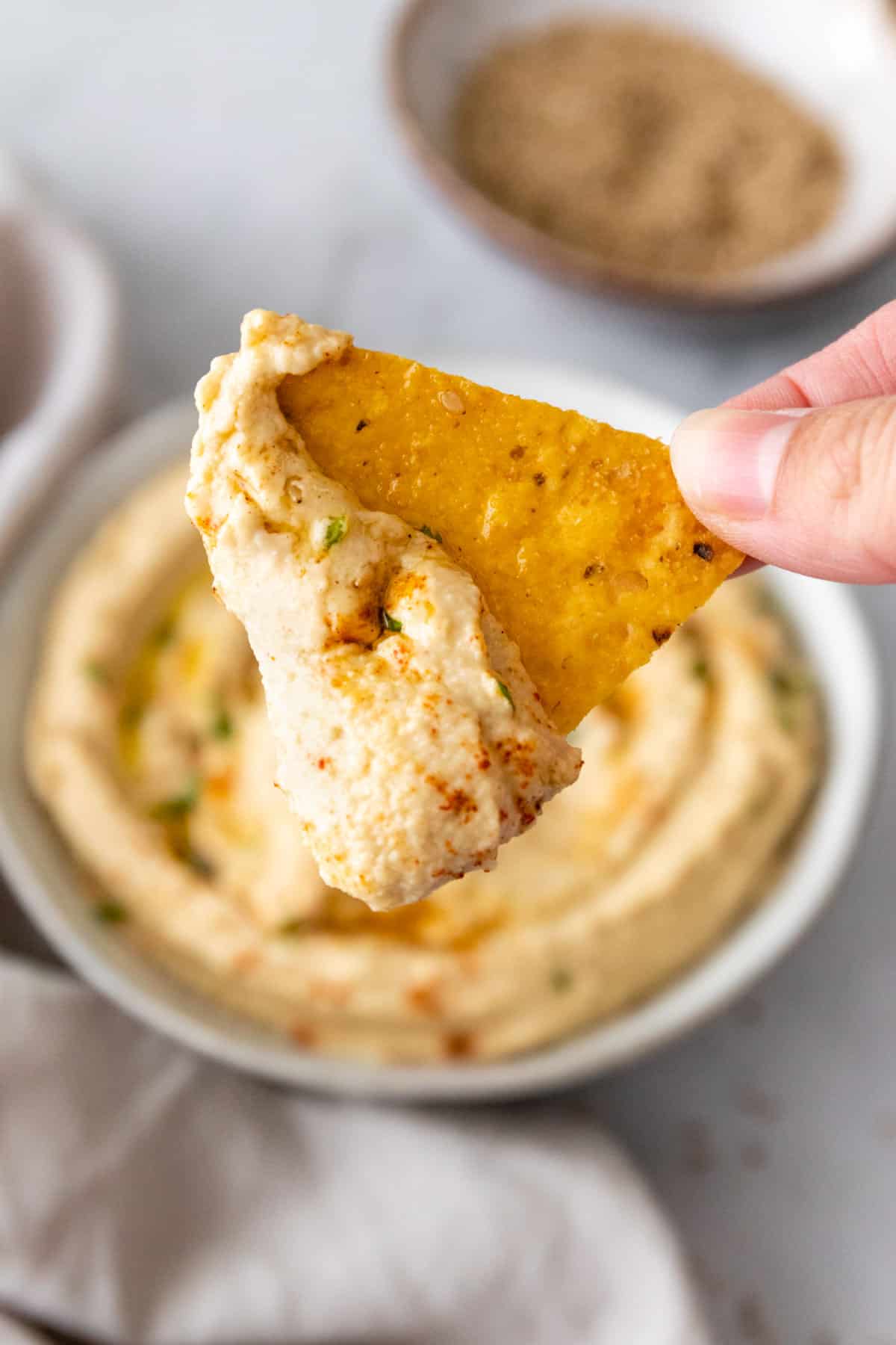 two fingers holding a chip with hummus