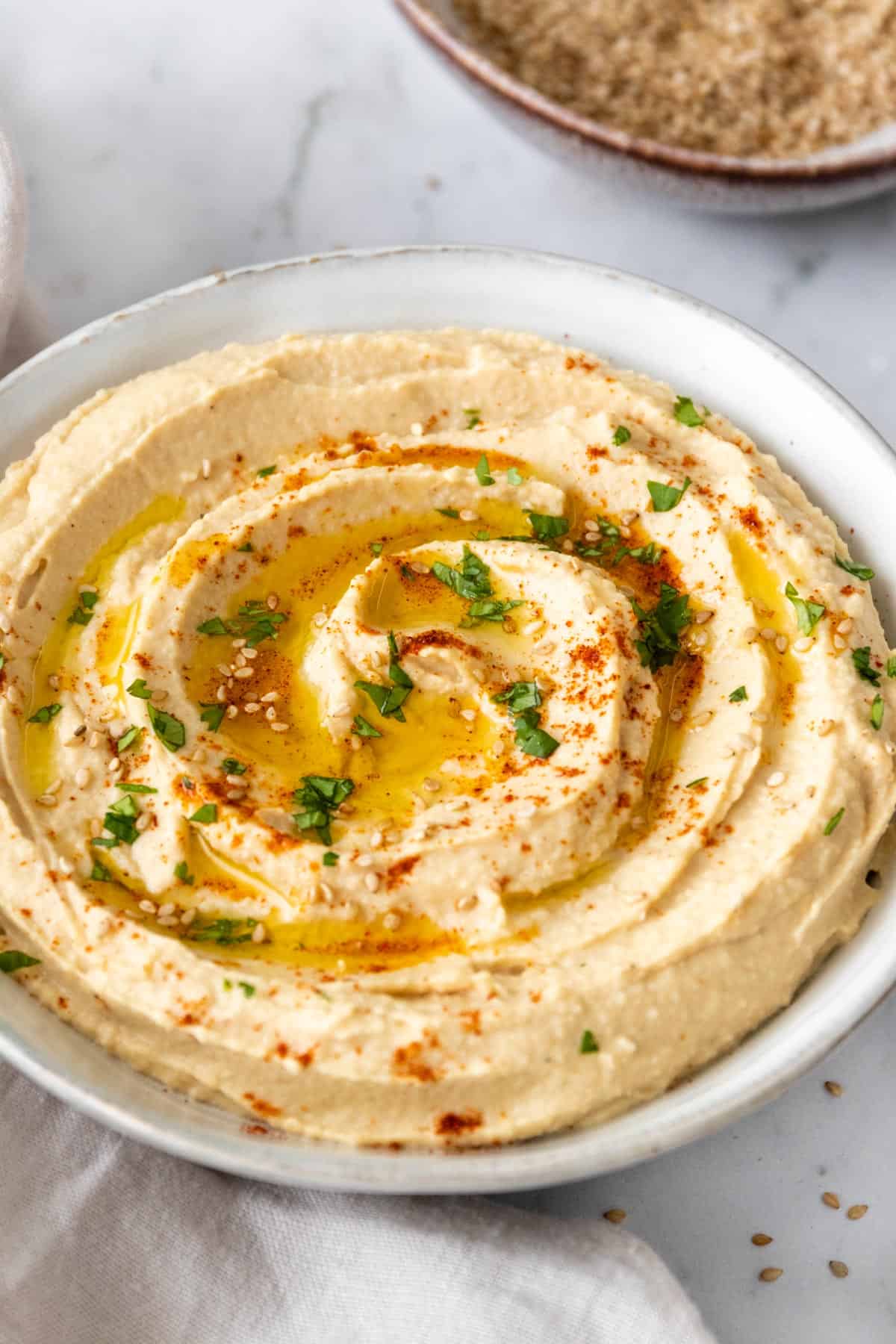 a bowl with hummus garnished with sesame seeds, olive oil, paprika, and chopped parsley